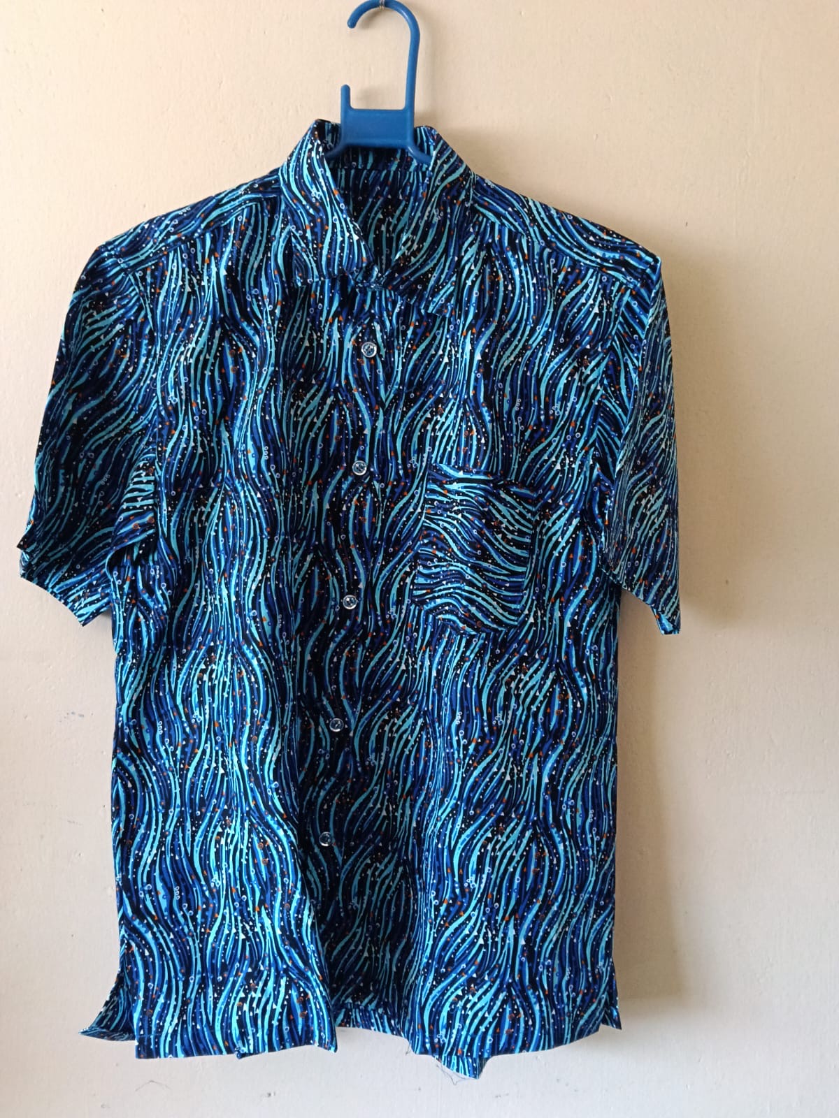 Blue Wave-Print Short-Sleeve Shirt — A collared short-sleeve shirt in layered navy and turquoise wave-like print, finished with a chest pocket.