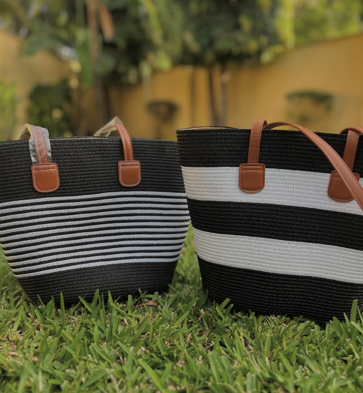 Black and White Striped Woven Totes — A pair of hand-woven totes in bold black and white striping, finished with tan leather handles.
