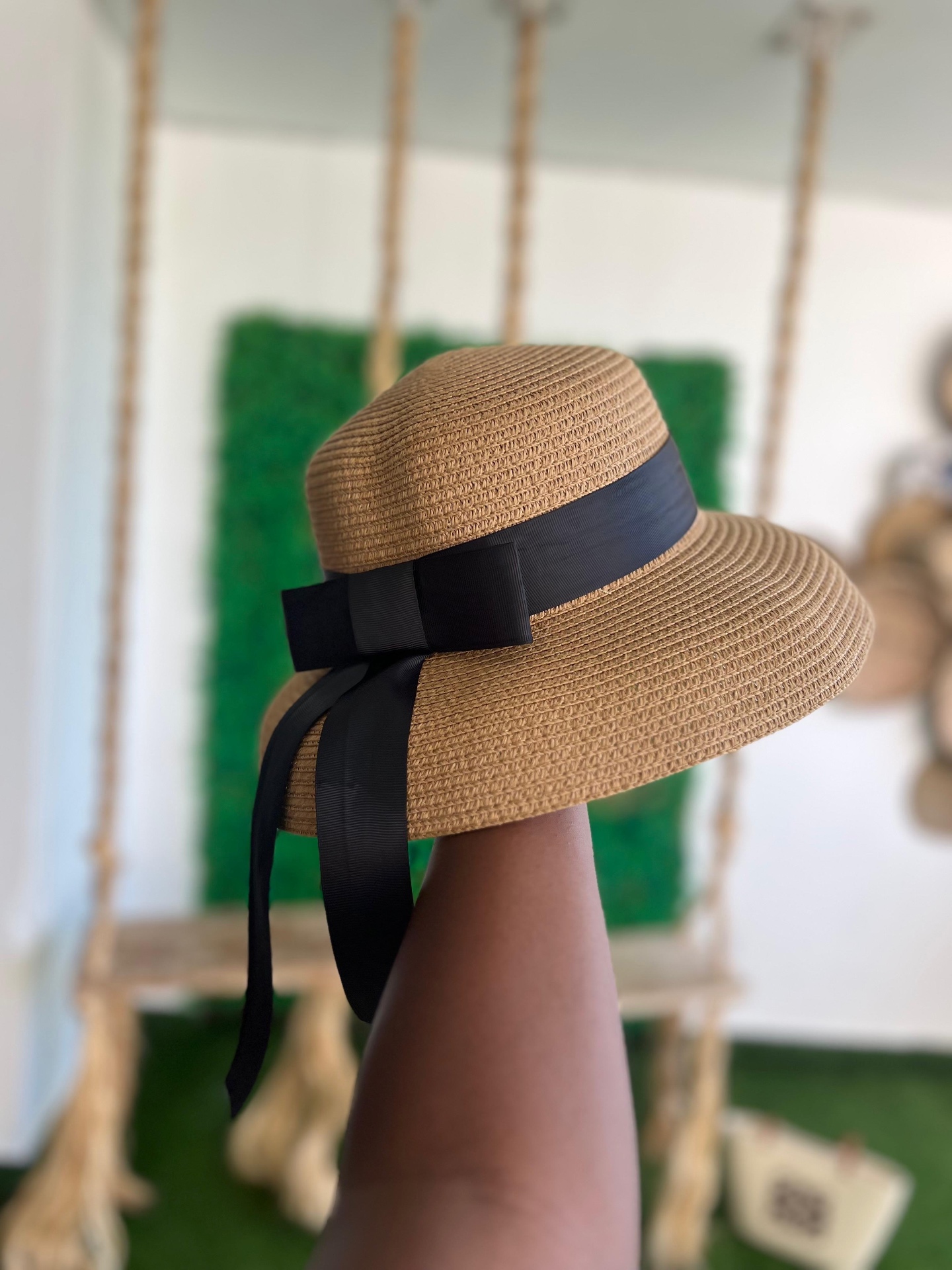 Wide-Brim Straw Hat with Grosgrain Ribbon — A woven straw sun hat with a downturned brim, banded in black grosgrain and tied in a long trailing bow.
