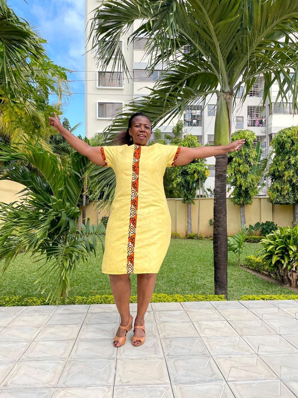 Sunshine Cotton Dress with Orange Kitenge Placket — A softly tailored yellow cotton day dress with a hand-set orange kitenge placket running the full length of the front, repeated on the sleeve cuffs.