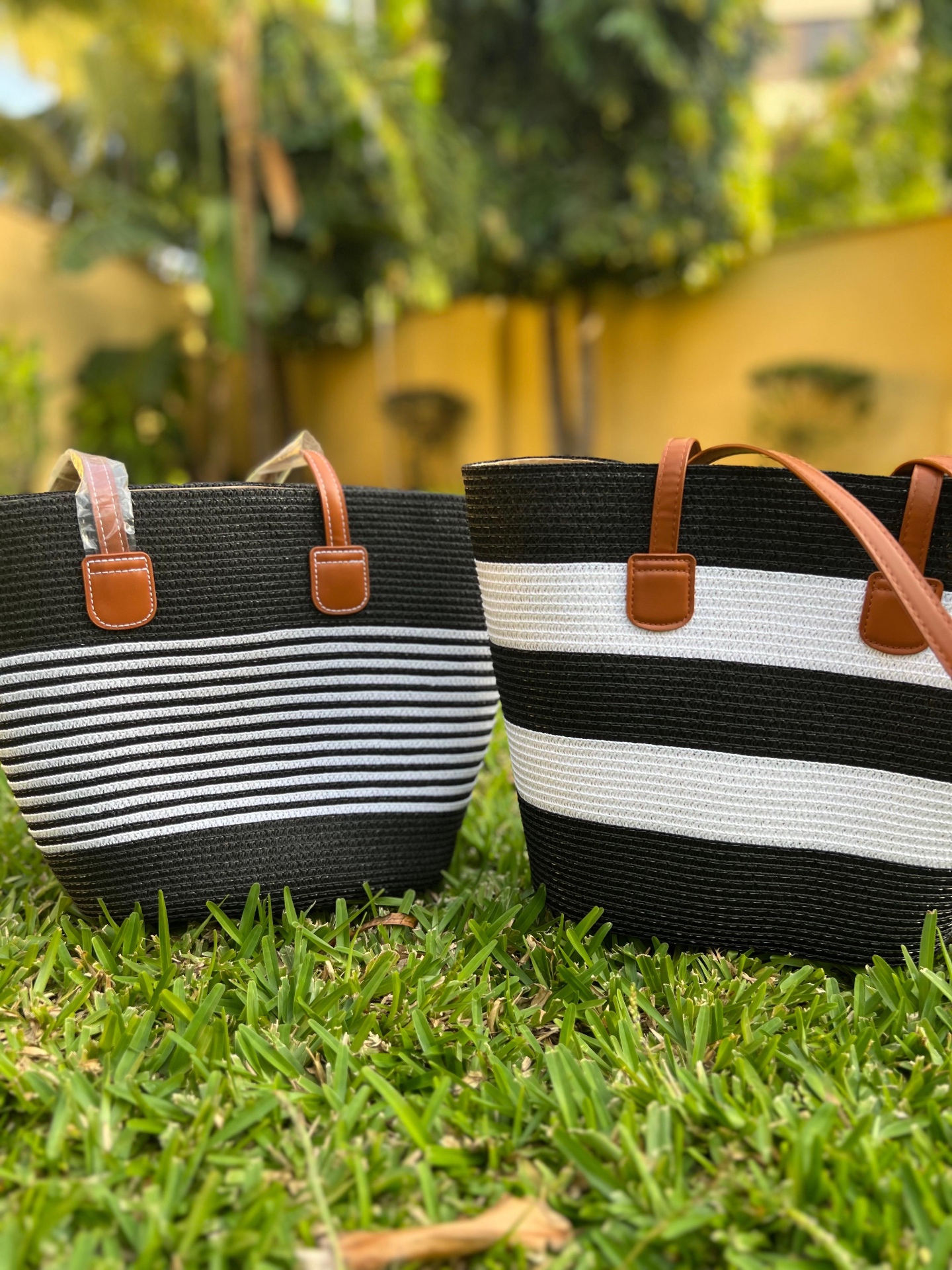 Striped Woven Tote with Leather Handles — A structured hand-woven tote in bold black and ivory stripes, finished with tan leather handles and stitched tab fittings.