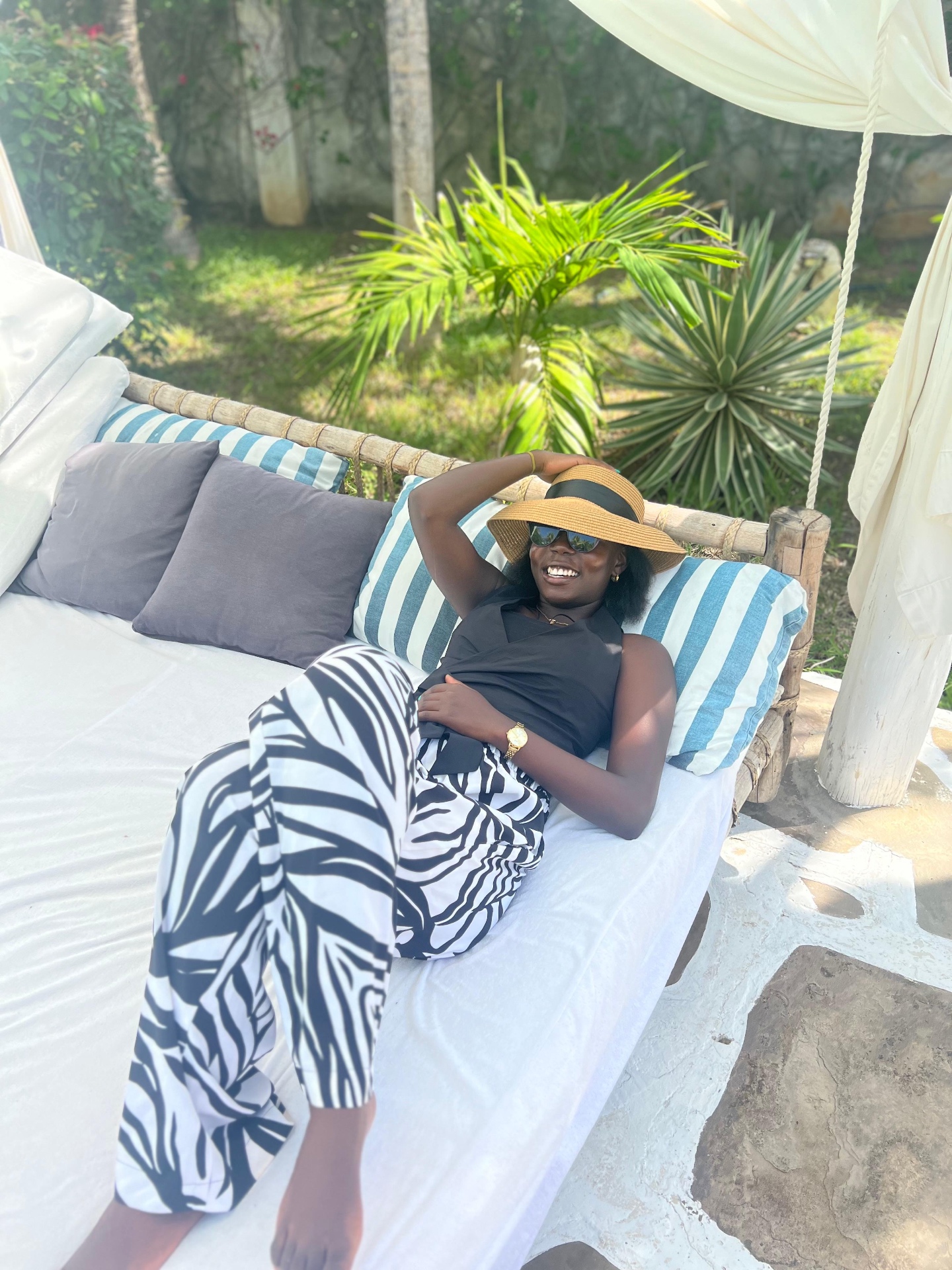 Monochrome Palm-Print Wide-Leg Trousers — Fluid wide-leg trousers in a black and white palm-frond print, cut for coastal heat and worn here with a straw brim hat.