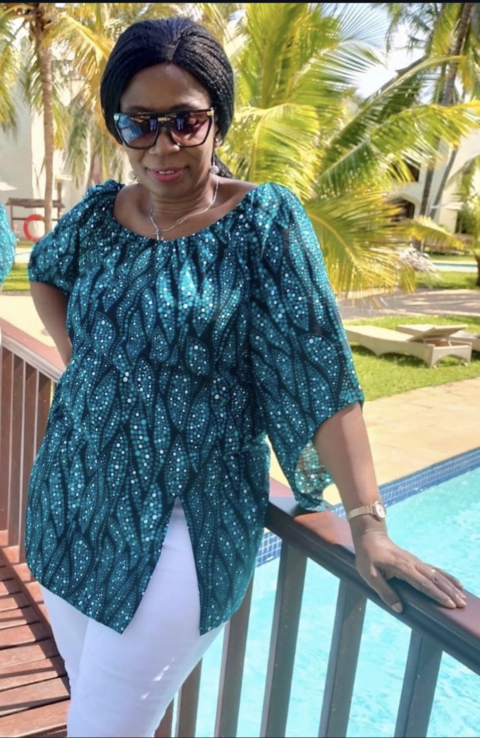 Teal Wave-Print Blouse — A relaxed blouse in a teal wave-and-dot print with a gathered neckline and three-quarter sleeves, worn here with white trousers.