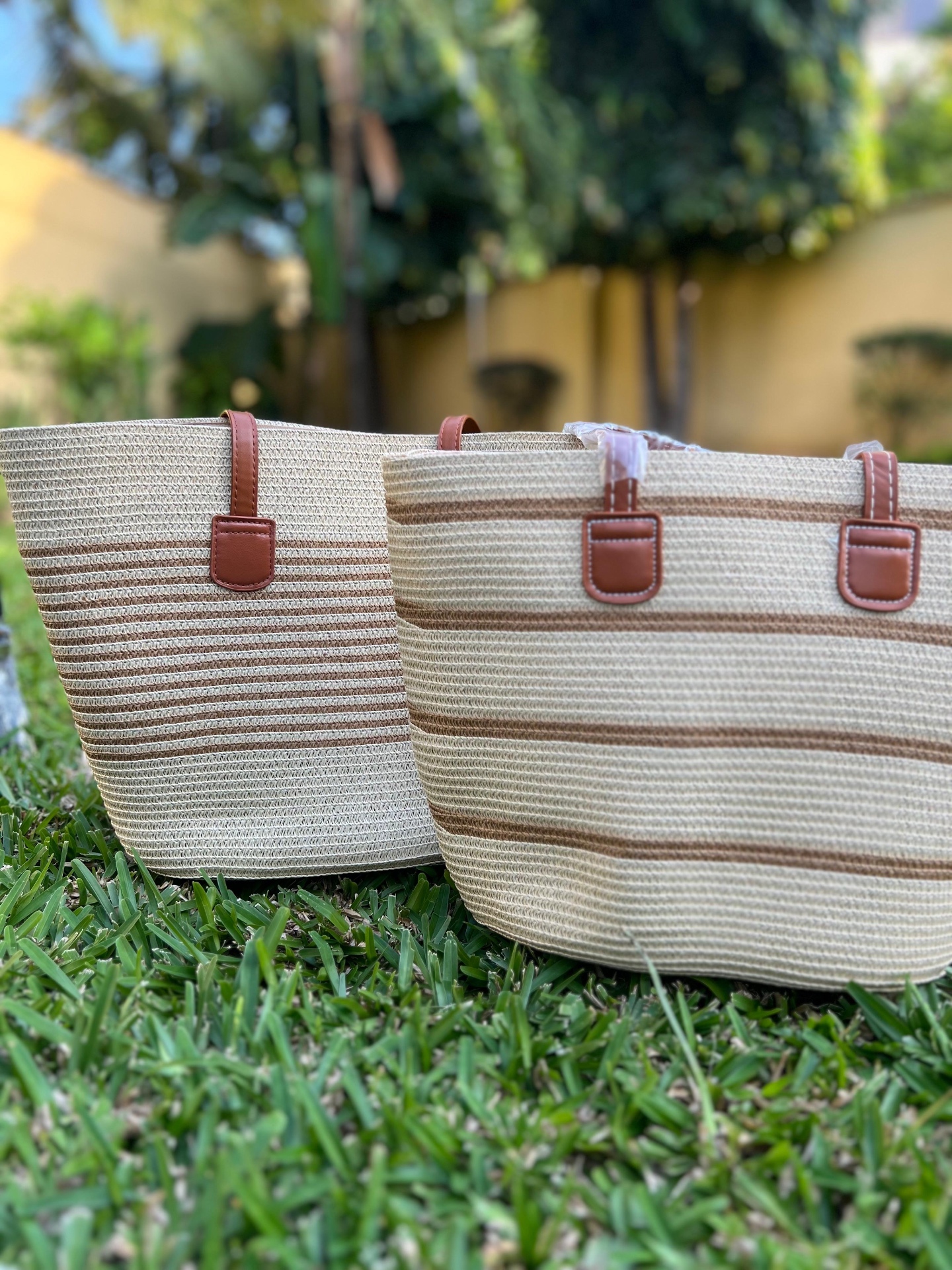 Natural Woven Tote with Cocoa Stripe — A softly rounded market tote woven in natural straw with cocoa banding, carried on tan leather handles.