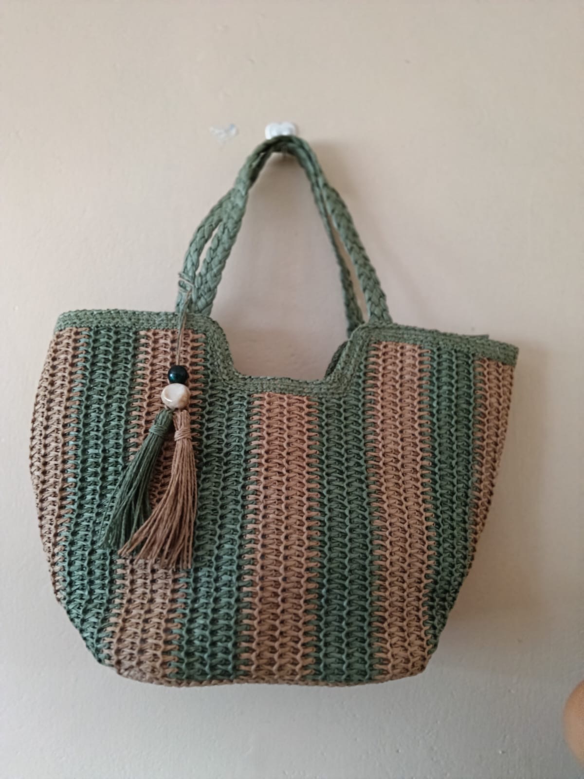 Green and Taupe Striped Woven Tote — A softly structured woven tote in alternating green and taupe stripes, finished with braided handles and a tassel.